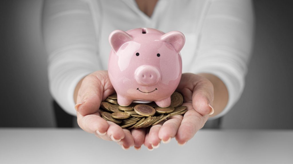 na imagem vemos uma mulher segurando um cofrinho em formato de porco e várias moedas para representar a economia que se faz com a técnica explicada no artigo.